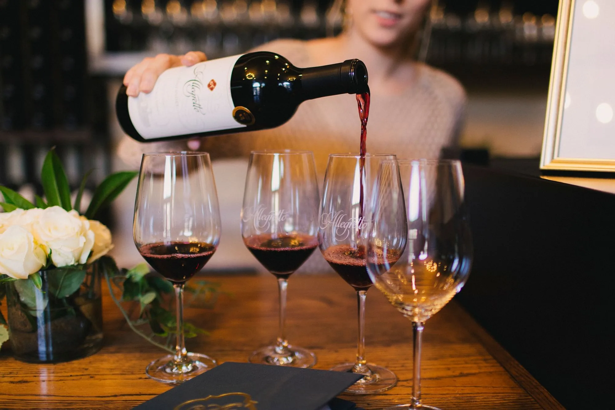 Allegretto wine being poured into a row of Allegretto-etched glasses on a wood table