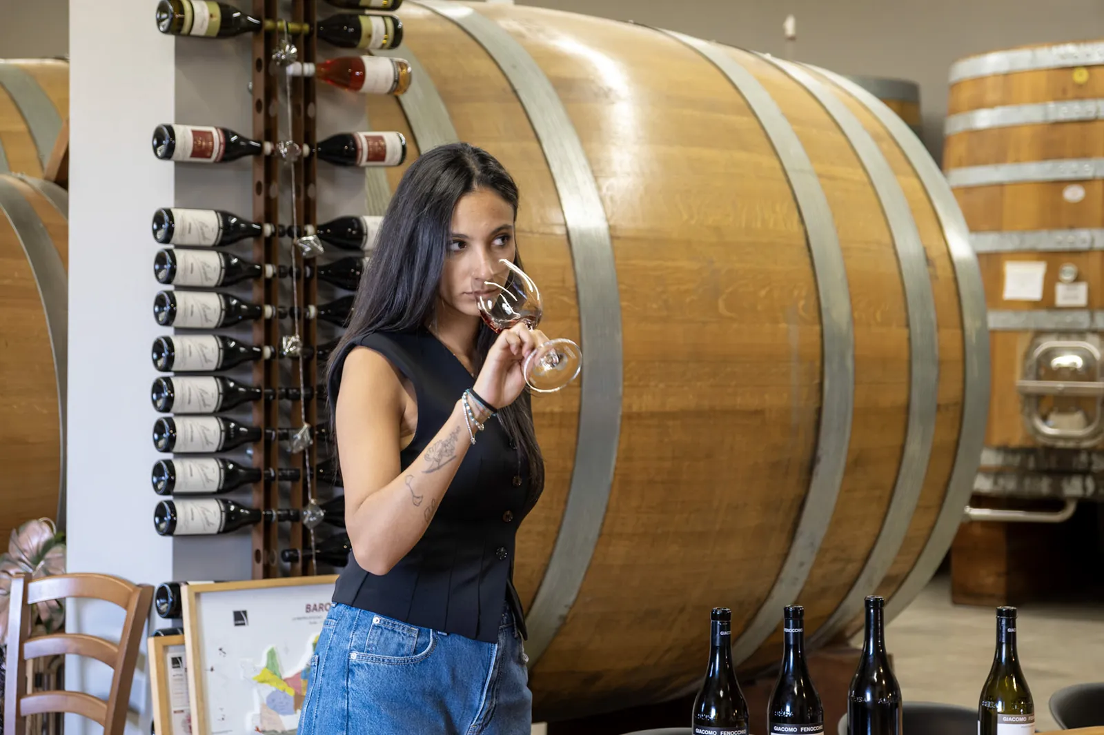 Letizia Fenocchio nosing a glass of red wine in front of large oak casks in the Giacomo Fenocchio cellar